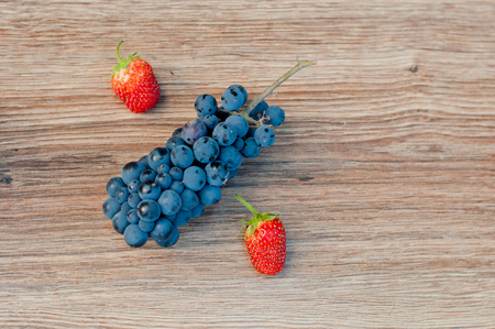 Symbol percent made of blue grapes and red strawberries on brown wooden background. Top view. Space for textの写真素材