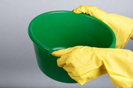 Human hands in yellow rubber gloves hold green washbowlの写真素材