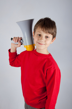 Smiling child in red pullover holding loudspeaker on his shoulder. Bright backgroundの写真素材