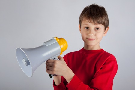 Cute boy holding megaphone in his hands on bright backgroundの写真素材