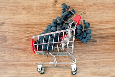 Bunch of blue grapes in small metal shopping cart laying on brown wooden table. Top viewの写真素材