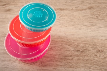 Heap of round plastic containers on wooden table. Magenta, orange, blue color, different sizes. Space for textの写真素材