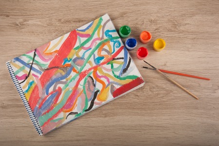 Abstract multicolored gouache picture on paper, brushes and paintings on wooden tableの写真素材