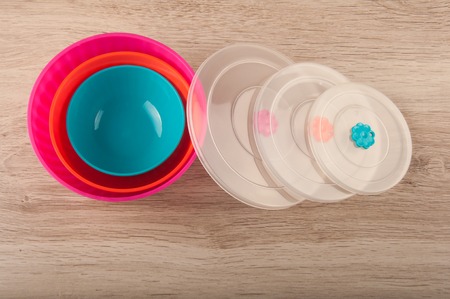 Three round plastic lunch boxes and transparent covers lay on wooden table. Magenta, orange blue colors and different sizesの写真素材