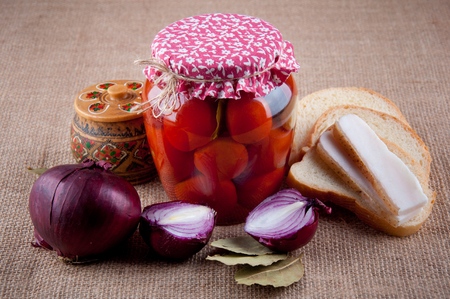 Authentic ukrainian Still Life. Transparent glass jar with tomatoes inside covered by red cloth, red onion, wooden round box with pattern, slices of bread and lard, bay leaves lay on sackcloth as backgroundの写真素材