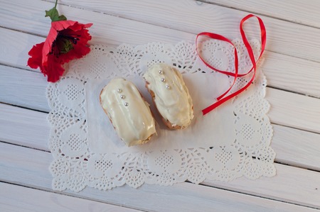 confectionery. Two white chocolate eclairs with silver balls and red poppy flower, ribbon lay on...