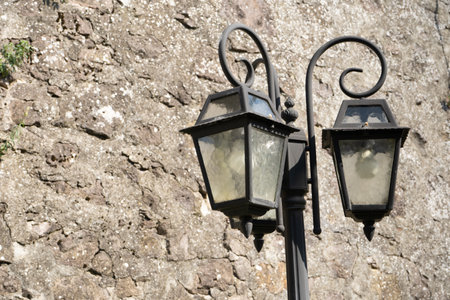 Old vintage street lamp, glass lantern and black iron decorations on light brown stone wall...