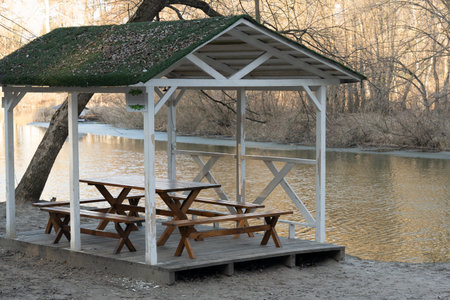 Wooden deck and columns of a gazebo with table, bench for picnic overlooking a calm river with trees in the background. Relax in nature, camping. High quality photoの写真素材