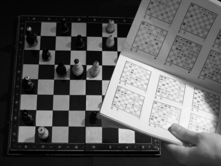 Hand holding book about chess and chessboard behind itの写真素材