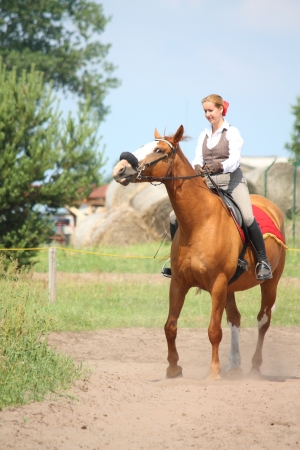 Beautiful young blonde woman riding trotting chestnut horseの写真素材