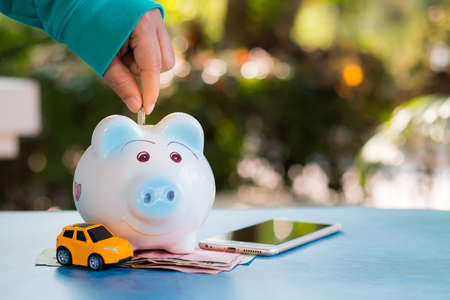 Savings deposit coins in a clear glass bottle, on a wooden floor with bokeh in the background.の写真素材