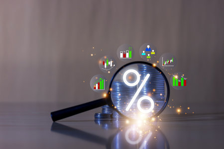 Magnifying glass highlighting a percentage symbol over coin stacks with financial chart icons. Concept of interest rate, investment, and economic analysis.の写真素材