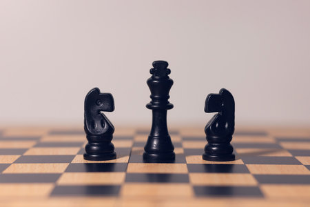 Black chess king with two knights on wooden chessboard, symbol of leadership, teamwork, strategy,...