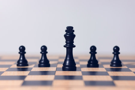 Black chess king surrounded by pawns on wooden chessboard, symbol of leadership, teamwork, business strategy, authority, and competition concept.の写真素材