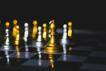 Golden pawn standing among silver pawns on chessboard symbolizing leadership, success, individuality, and business strategy.の写真素材