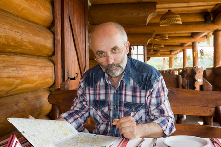 Middle-aged man with glasses at the table in a roadside restaurant is considering road mapの写真素材