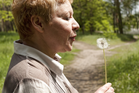 Middle-aged woman in profile blowing a dandelionの写真素材