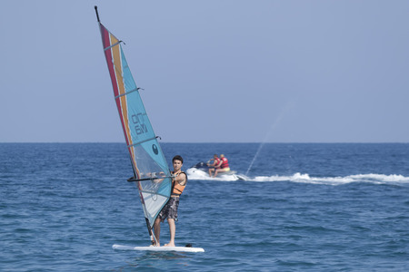 CAMYUVA, KEMER, TURKEY - JULY 11, 2015: Unidentified Turkish man glides over the waves of the Mediterranean Sea windsurfing. Extreme water sports are increasingly popular on the beaches of Turkeyのeditorial素材