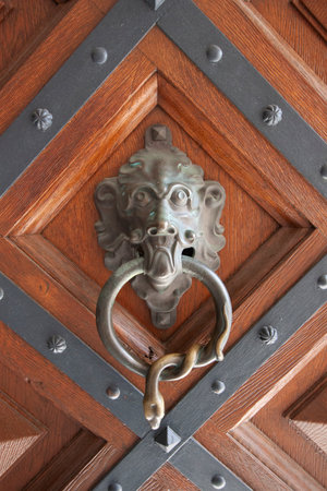 A detailed, close-up shot of an antique door knocker featuring a grotesque face with a ring handle,...