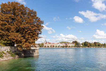 A picturesque wide-angle view of the tranquil Lake Constance (Bodensee) waterfront in Konstanz, Germany, under a bright blue sky with scattered white cloudsの写真素材