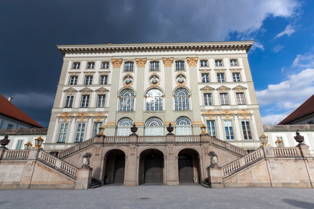 MUNICH, GERMANY - MAY 17, 2025: A grand and imposing front-on view of the magnificent Nymphenburg Palace in Munich, Germany, under a dramatic sky with both dark storm clouds and patches of blueの写真素材