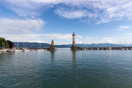 A wide-angle view of the iconic harbor entrance of Lindau on Lake Constance (Bodensee), Germany, under a bright blue sky with scattered cloudsの写真素材