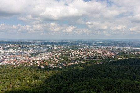 Aerial view of Stuttgart city and green forest on a sunny day with fluffy clouds. The cityscape stretches out under a clear sky, highlighting a beautiful blend of urban and natural landscapesの写真素材
