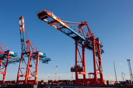 HAMBURG, GERMANY - AUGUST 12, 2024: Massive red container cranes standing tall against a clear blue...