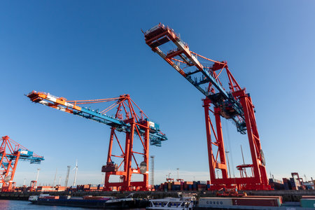 HAMBURG, GERMANY - AUGUST 12, 2024: Massive red container cranes standing tall against a clear blue...