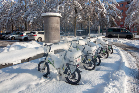 RAVENSBURG, GERMANY - DECEMBER 3, 2023: Row of rental bicycles completely covered in thick fresh snow at a docking station during a sunny winter day. Urban mobility affected by heavy snowfallのeditorial素材