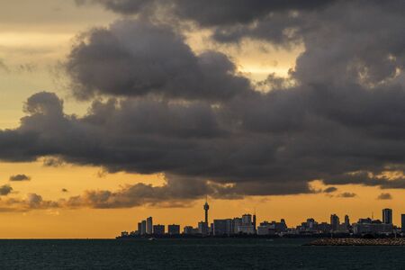 Cityscape, landscape, view of sea with a city at the horizon at twilight before sunset. View of Pattaya city from    Jomtien Beach with orange sky and heavy black cloud.の写真素材