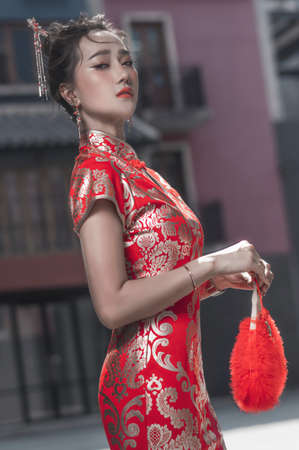 Beautiful Asian woman, model,  wearing traditional red cheongsam qipao dress holding red foldable...