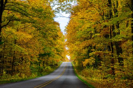 Gorgeous display of fall colors, leaves, red, orange, green and yellow trees with both side of empty road leading your eye through the picture. Pictured Rocks National Lakeshore, Munising, MI, USAの写真素材