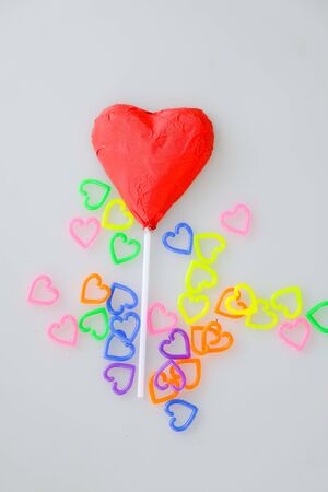 Heart shaped chocolate candy with red wrappings and colorful mini  heart toy plastic on white backgroundの写真素材