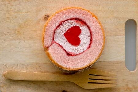 Cake roll with strawberry marmalade jam and jelly shape heart on wood with wood fork.の写真素材