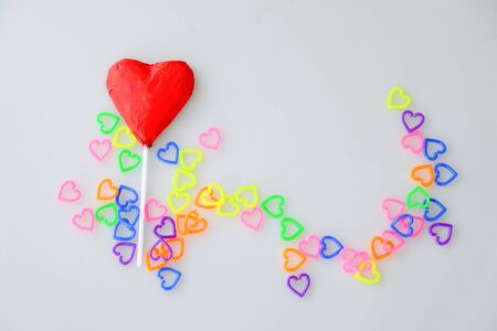 Heart shaped chocolate candy with red wrappings and colorful mini  heart toy plastic on white backgroundの写真素材