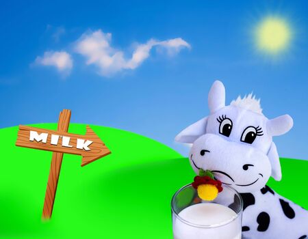 Cute toy cow with a glass of milk and sunny sky in the backgroundの写真素材