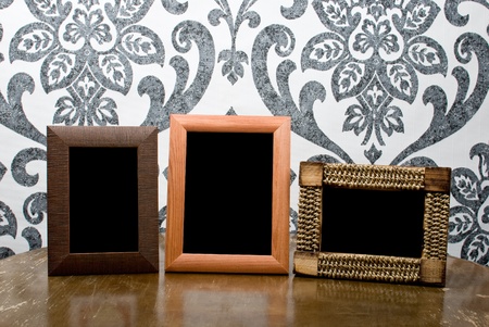 Three wooden photo frames on old table on vintage wallpaper backround