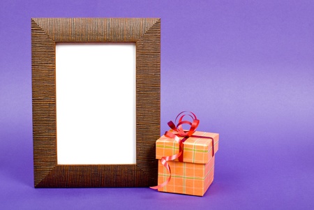 Wooden photo frame and orange gift box with red ribbon on blue background.の写真素材