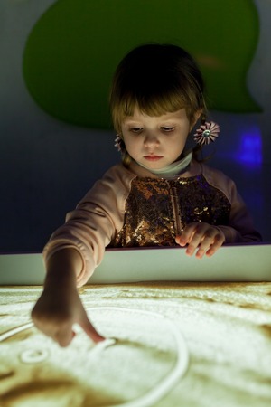 Girl in the game draws her fingers on the sand with a backlightの写真素材