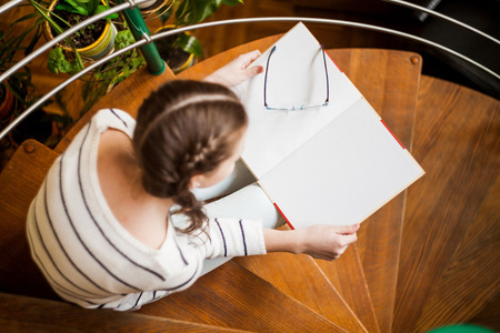 Top view shot of a happy young beautiful woman sitting on the stairs reading a book enjoying studying copyspace education college campus high school university intelligence hobby.の写真素材