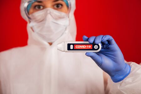 Coronavirus. The New Coronavirus COVID-19. A woman in a mask on a red background with a coronavirus reads its temperature on a thermometer with the inscription COVID-19.の写真素材