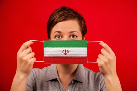 Coronavirus COVID-19 in Iran. Woman in medical protective mask with the image of the flag of Iran. The concept of preventing the spread of the epidemic and treating coronavirus.の写真素材