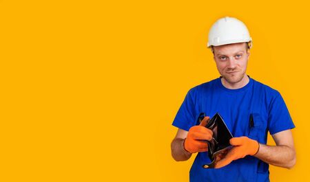 The puzzled worker in overalls holds his empty purse without money. The concept of economic crisis,...