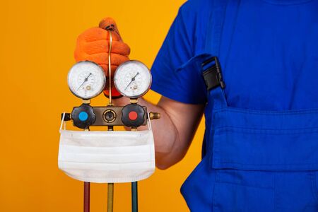 An air conditioning technician holds pressure gauges in his hand for refueling air conditioners. Medical face shield on measuring equipment for filling air conditioners.の写真素材