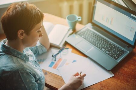 Working at home. Woman accountant analytics doing chart analysis in business, sitting at the table with laptopの写真素材