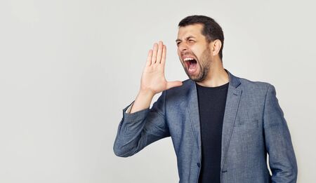 A young man with a beard screams out loud with his hand near his mouth.