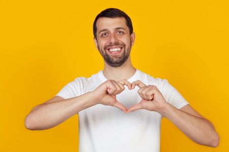 Handsome young man, smiles and makes a heart-shaped symbol with his finger
