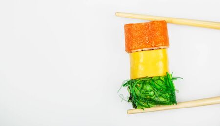 Sushi roll with chopsticks, with cucumber kappa maki roll. Japanese kitchen. Various sushi and rolls with fish cheese and with chuka salad in chopsticks isolated on a white backgroundの写真素材