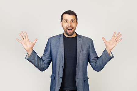 Young businessman man with a beard in a jacket, celebrating crazy and amazed with success with raised hands and open eyes, shouting excitedly. Winner concept. Portrait of a man on a gray background.の写真素材
